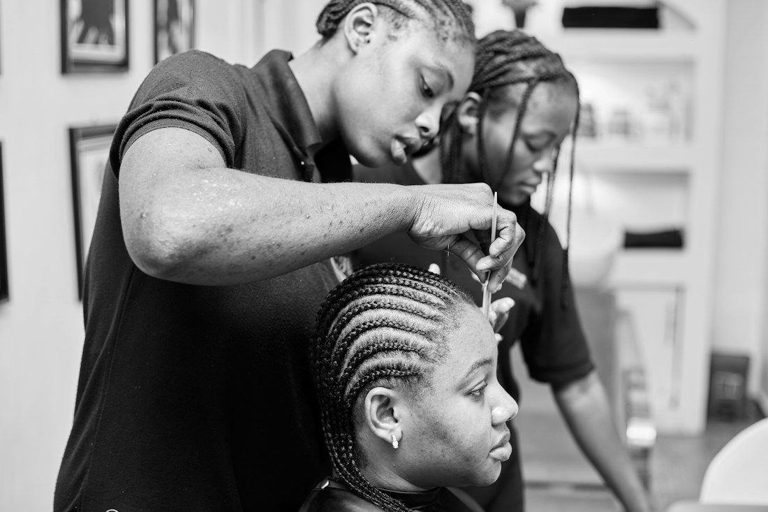 Two hairstylists braiding a customer's hair in a salon.